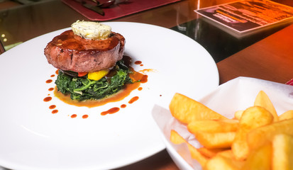 Beef steak served with french fries and spinach topped with sauc