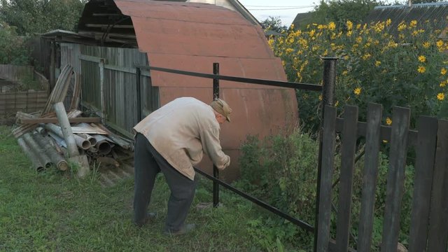 Old man 70s paints the iron fence using a black