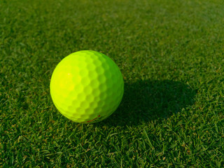 Isolated bright green golf ball site on golf course grass waiting for player to putt into hole for par score. Morning sunrise shadow cast on fairway. Low Angle