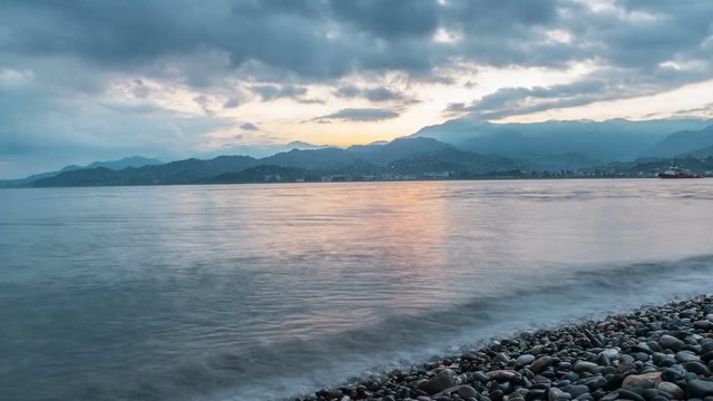The time before the sun rises near the ocean. Beautiful mountains and clouds are illuminated in orange rising sun. Wieden rocky beach Georgia