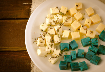 Cheese platter, Gouda, feta, blue pesto cheeses on white plate with herbs, olive oil, pomegranate and mustard sauces