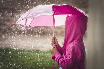 A young girl is holding a pink umbrella in a massive rain storm.