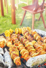 Meat skewers with onions and corn cobs in aluminum foil, garden barbecue, selective focus.
