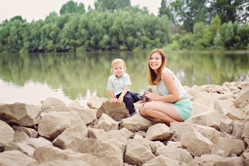 Mother and son sit on the stony banks of the river, full length.