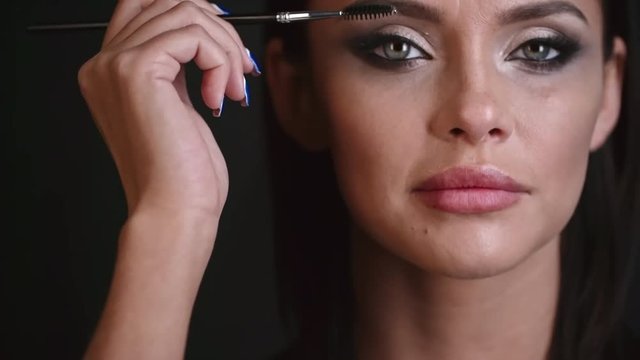 Closeup of woman with professional makeup brushing her eyelashes and then looking at the camera and smiling