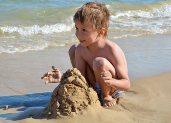 Мальчик играет с песком у моря