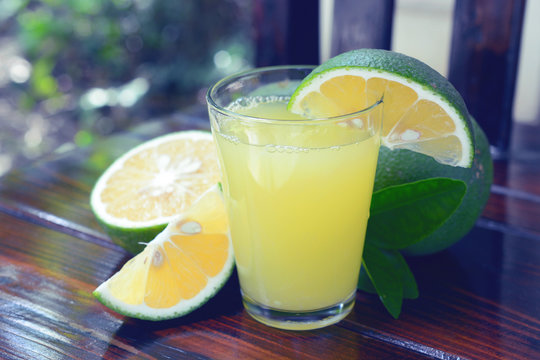 Fresh sweet orange juice with green peel (citrus senesis, citrus sinensis) on wooden background.