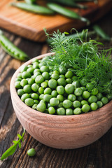 Green peas in wooden bowl on  rural background
