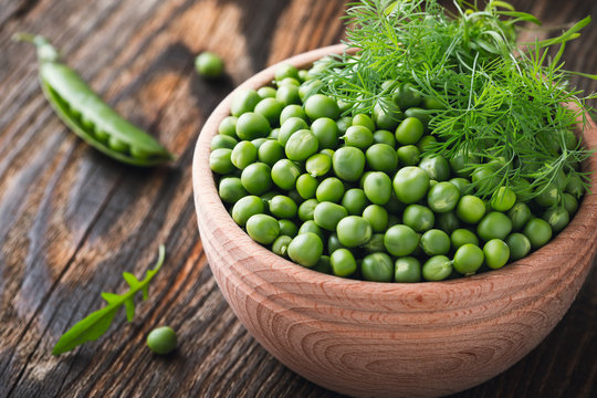 Green peas in wooden bowl on  rural background