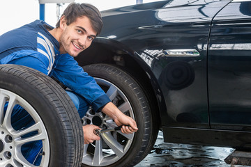 Fototapeta na wymiar Confident Mechanic Changing Car Tire At Automobile Shop