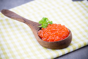 Salmon caviar with spoon on gray background.