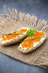 Bread with fresh cream cheese and red caviar on table.
