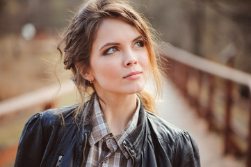 autumn outdoor portrait of young beautiful woman with natural makeup in leather jacket and plaid shirt, soft vintage toned