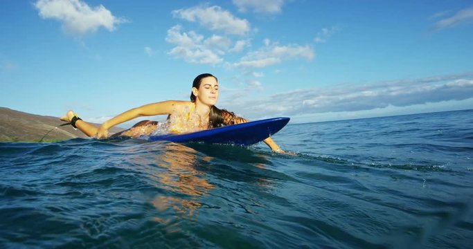 Beautiful surfer girl paddling into the sunset