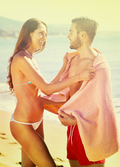 Happy couple standing in towel at sea coast