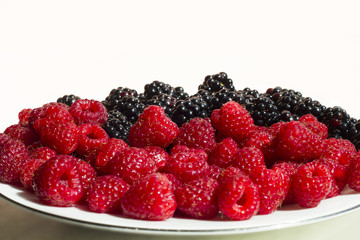 Fresh raspberries and blackberries on plate isolated on white background