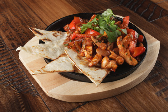 Fajitas with chicken and bell pepper in a pan. Wooden background.