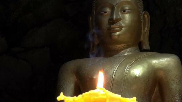 A Buddhist temple deep inside a cave.  A Buddha image is lit by a single flickering candle. 