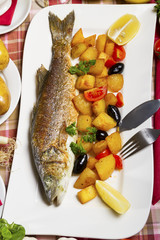 Fried sea bass with side dish on a plate, served on a table.