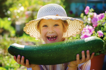 Little happy girl with zucchini in the hands of