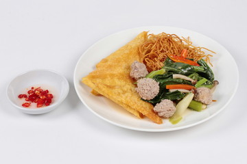 Crispy noodle topped kale soup with meatball and spicy sauce. Side view.