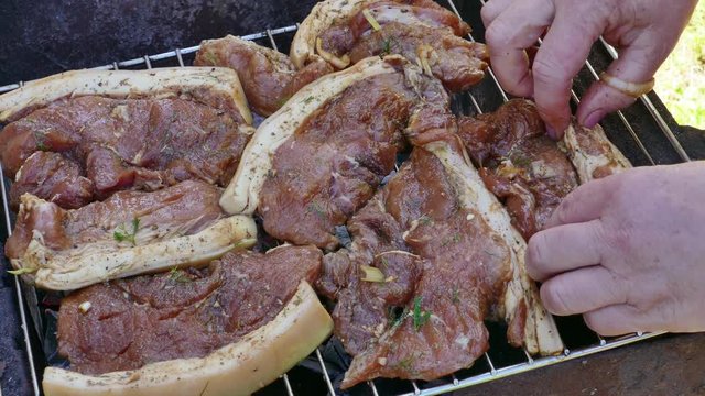 Hands Put Raw Pork Meat Steak on Barbecue Grill. Some Flames visible. Hand checking