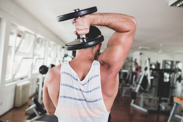 Young attractive adult man exercising and doing weight lifting at fitness gym. Sport training indoors.