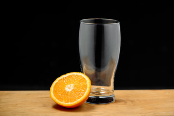 Empty glass with half orange on wooden desk. Copy space.