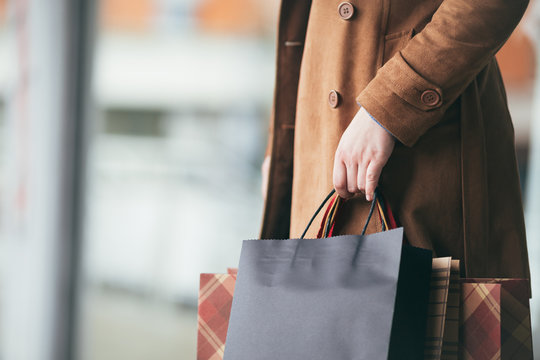 Elegant And Modern Woman In Brown Leather Jacket Or Topcoat Standing On The City Street And Holding Bunch Of Shopping Bags. Close Up Shot Of Woman Hand. Lifestyle Consumerism Theme. 