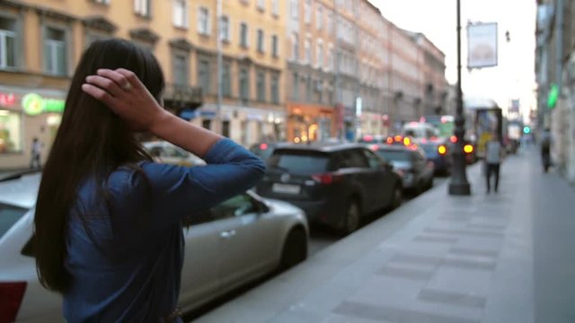 Backview of a girl at the street, flipping her hair back. Blurred background, city lights, cars, slow mo, steadicam shot