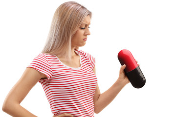 Sad young woman looking at a big pill