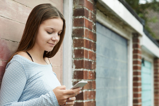 Teenage Girl Texting On Mobile Phone In Urban Setting