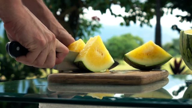 Female hands cutting melon on table in the garden, super slow motion
