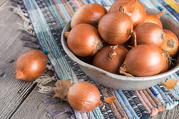 Onions.  Old bowl with onions on a homespun a mat on the wooden floor.