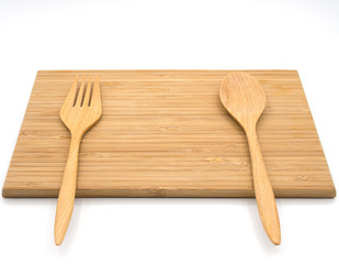 A wooden cutting board with wooden spoon and fork on the white b