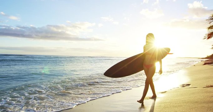 Beautiful surfer girl walking down the beach at sunset