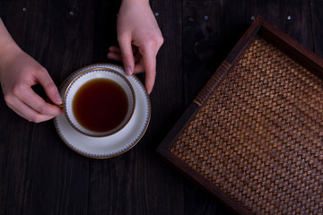 womans hands with cup of tea and rattan tray