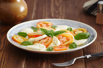 Caprese salad in a blue pastel plate on an old wooden table, with salt and pepper