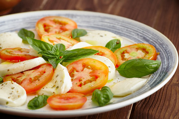 Caprese salad in a blue pastel plate on an old wooden table, with salt and pepper
