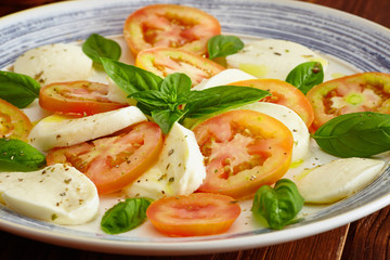 Caprese salad in a blue pastel plate on an old wooden table, with salt and pepper