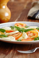 Caprese salad in a blue pastel plate on an old wooden table, with salt and pepper