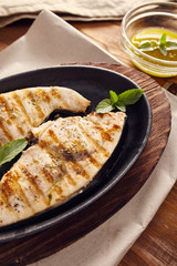 grilled swordfish slices in a cast iron pan on a wooden table, garnished with mint, oregano, salt and salmoriglio