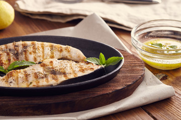 grilled swordfish slices in a cast iron pan on a wooden table, garnished with mint, oregano, salt...