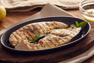 grilled swordfish slices in a cast iron pan on a wooden table, garnished with mint, oregano, salt and salmoriglio