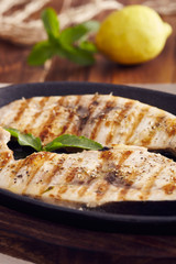 grilled swordfish slices in a cast iron pan on a wooden table, garnished with mint, oregano, salt and salmoriglio