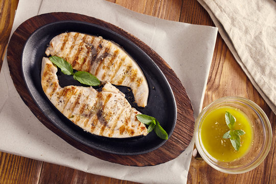 grilled swordfish slices in a cast iron pan on a wooden table, garnished with mint, oregano, salt and salmoriglio
