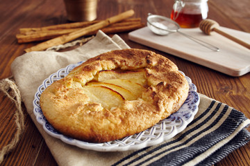 handmade apple pie on a dish over a napkin in a country style, cinnamon and hony in the background
