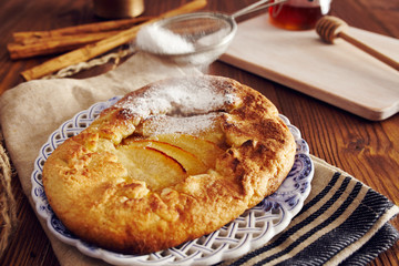handmade apple pie on a dish over a napkin in a country style, cinnamon and hony in the background