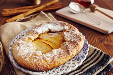 handmade apple pie on a dish over a napkin in a country style, cinnamon and hony in the background