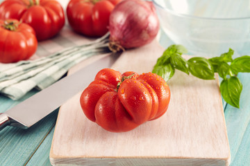 Tomatoes corleone type for sauce on a aqua wooden table with basil and onion